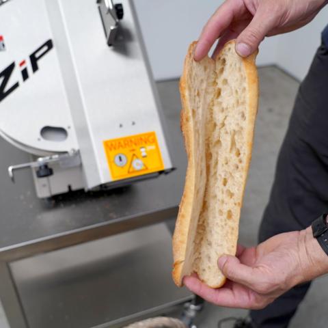 Broodsnijmachine Jac ZIP op de achtergrond en op de voorgrond een opengesneden stokbrood